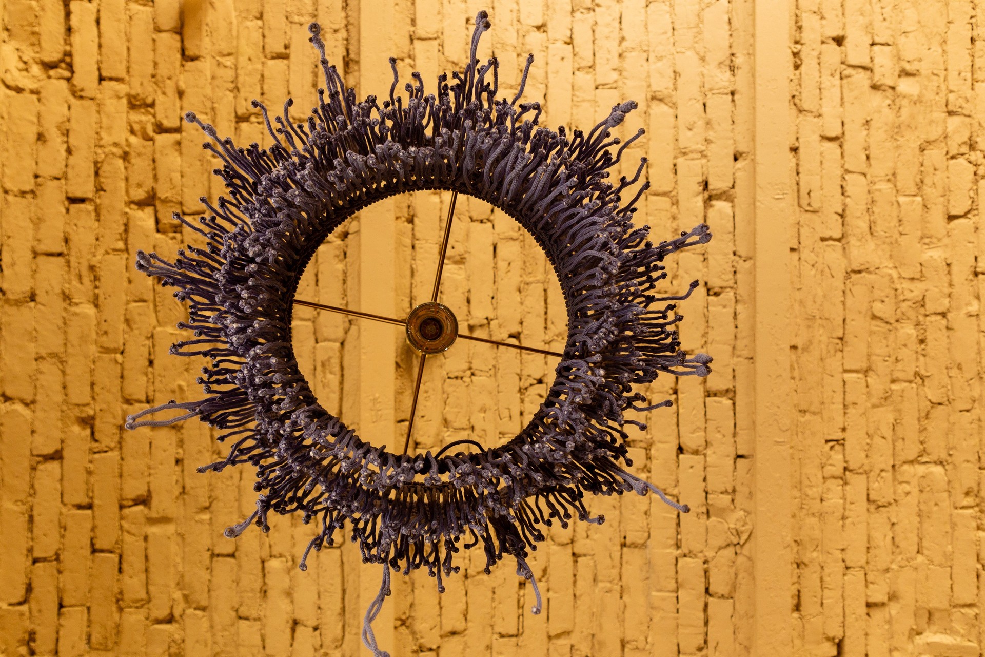 Macrame lampshade with fringes, suspended in front of a warm, background.